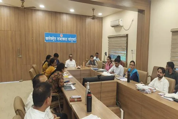 कलेक्टर सभाकक्ष पांढुर्णा में लकड़ी की लंबी मेज के दोनों ओर बैठे अधिकारी और महिला कर्मचारी, सामने फाइलें और कागज रखे हैं, दीवार पर 'कलेक्टर सभाकक्ष पांढुर्णा' लिखा नीला बोर्ड।